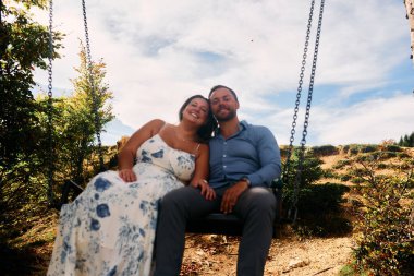 Dağlarda salıncakta sallanan bir çift, arka planda büyüleyici doğal manzarayla öpüşüyorlar. Seyahat, romantizm, yaşam tarzı ve macera temaları için mükemmel