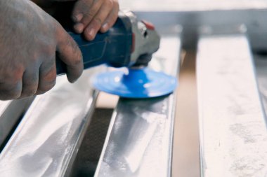 Close up of workers hand operating an angle grinder with blue disc to polish and smooth metal surface in industrial workshop