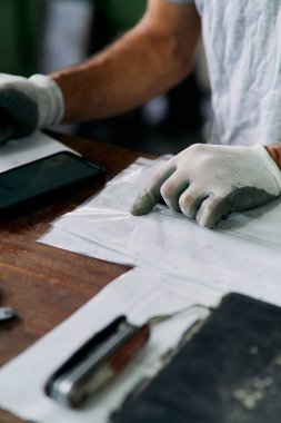 Close up of workers hands in white protective gloves reviewing technical documents and notes on wooden desk in industrial environment, symbolizing planning, organization, and quality control