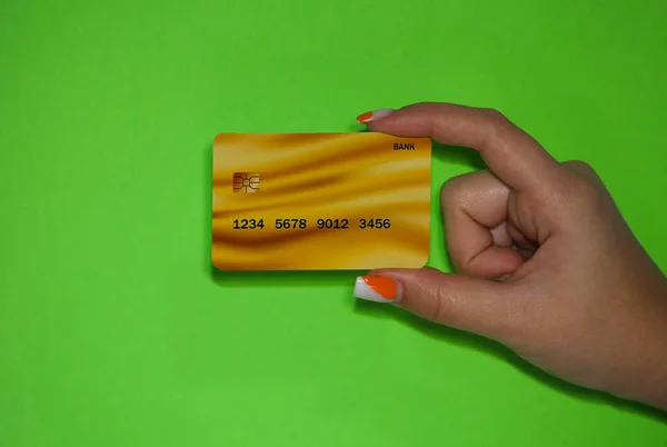 Picture of a womans hand holding a Gold card on a green background. The gold card is one of the rich cards. High quality photo