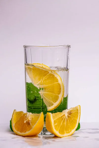 Picture on a white background with a glass that has a slice of lime in it and two halves of lime around it. lemon has an important role in human life. You can make different cocktails from lemon. High