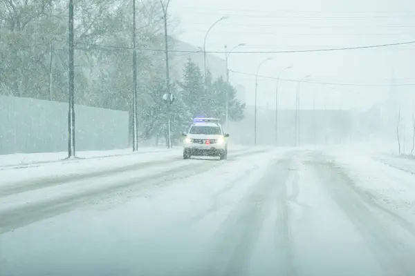 The picture of a police car that makes sure that everything is in order and that the drivers take care of the traffic rules because outside there is a yellow code for strong wind and snow. High