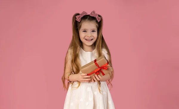 The little girl is very happy to have received an unexpected gift, and she is pictured enjoying this gift on a pink background. The girl has a very beautiful smile. High quality photo