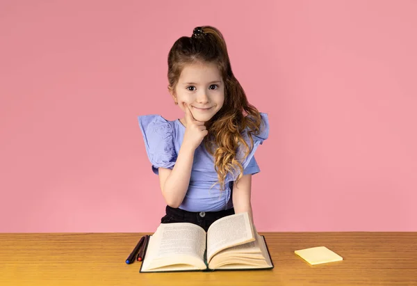 Resim pembe bir arka planda, kadın cinsiyeti için mükemmel bir renk, kız çok güzel giyinmiş ve iki güzel at kuyruğu var, kitap okurken çok şaşırmış ve...