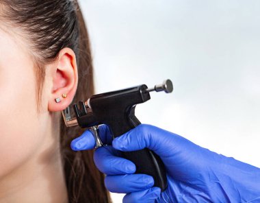 Güzellik merkezinde özel bir delici silahla kulak delme işlemi yapan bir kadın. Yüksek kalite fotoğraf
