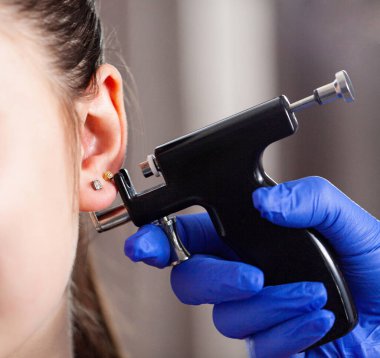 Uzman, müşterilerin kulaklarını delici bir silahla deliyor. Beyaz kadın kulak delme işlemi geçiriyor. Kuaförde güzellik prosedürü. Yüksek kalite fotoğraf