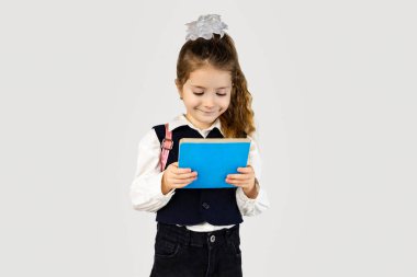 Küçük kız elinde elektrikli mavi bir tablet tutuyor, yüzünde bir gülümsemeyle. Resmi bir kıyafet giyiyor, yaka ve kollarıyla, özel bir etkinlikte baş parmak hareketi yapıyor.