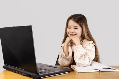 Genç bir kız dizüstü bilgisayarı olan bir masada otururken gülümsüyor, bir çıkış cihazı. Masa ofis malzemeleriyle dolu ve insan vücudu rahat bir şekilde yerleştirilmiş.