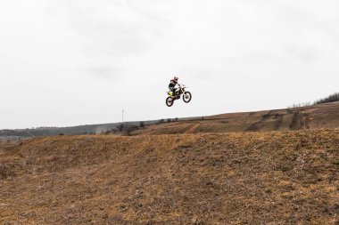 Bir dublör motorsiklet sporu disiplininde yeteneklerini sergiledikleri bir motokros yarışı sırasında gökyüzünde toprak bir motosiklet üzerinde bir numara yürütür.