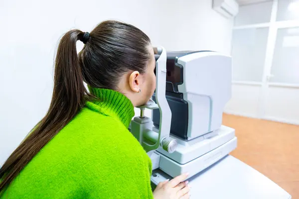 A woman with a green sweater is examining a machine in an engineering building. She seems focused and attentive to her job in the field of science and technology