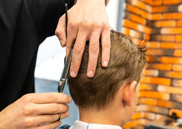 Erkek berber, tarak ve makas kullanarak küçük çocukların saçını kesiyor. Çocuğun saçlarını yetişkin bir erkekten kestiriyor, muhtemelen berber. Modern berber dükkanında profesyonel kuaför ve şirin bir müşteri. Yüksek kalite fotoğraf