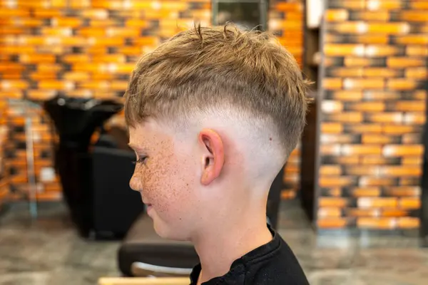 The picture of a small child in a barbershop studio, taken from the side and enjoying the beautiful haircut and the new style, the child has blue eyes and freckles. High quality photo