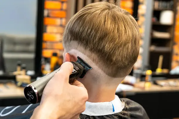 Shooting in a beauty salon. A barber cuts the hair of a little boy with a machine. High quality photo