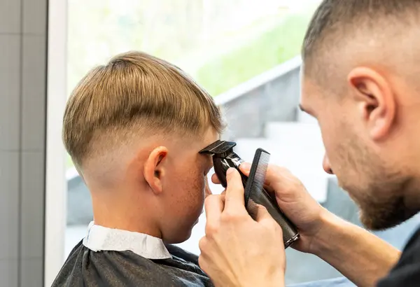 Erkek eli, berber dükkanında çocuk saçı tarıyor. Kuaför makinesiyle kesilmiş bir çocuk. Berber dükkanında saçını kesmek için erkek çocuk portresi. Yüksek kalite fotoğraf