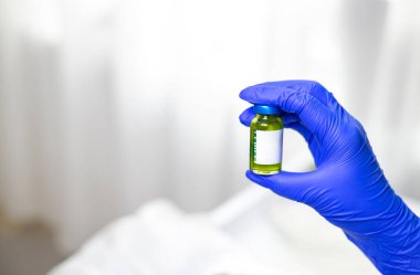 Küçük cam bir şişede sarı kozmetik solüsyon tutan lastik eldivenli bir elin yakın plan fotoğrafı. Kozmetik ilaç, güzellik tedavileri, cilt bakımı. Yüksek kalite fotoğraf