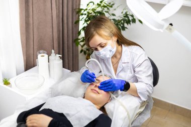 Kozmetik uzmanı deri kalemini elinde tutuyor ve müşterisine mikro cilt bakımı uyguluyor. Müşteri ameliyat masasında yatan genç bir kadın. Yüksek kalite fotoğraf