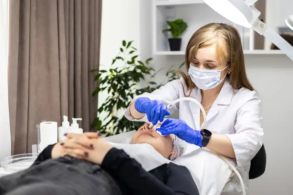 Cilt bakımı uzmanı müşterisinin yüzünde sivilce ve burun kenarındaki siyah noktalara karşı mikro cilt bakımı yapıyor. Güzellik salonunda kadın kozmetolojisi. Yüksek kalite fotoğraf