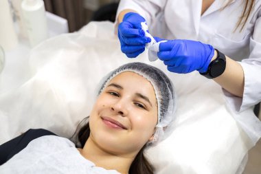 Masaj masasında ya da spa yatağında yüz masajı yaptıran ve yüz bakımını tazeleyen bir kadın. Kozmetik uzmanı kadın yüzünden yüz maskesi çıkarıyor. Yüksek kalite fotoğraf