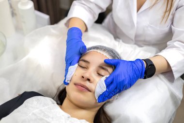 Azot eldivenli cildiyeciler, kağıt mendil kullanarak genç kadınların yüzündeki jöle kalıntılarını temizliyor. Yüksek kalite fotoğraf