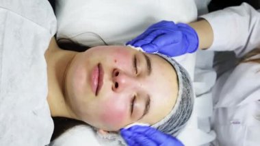 SPA tedavileri, yüz yenileme. Bir kozmetolog, bir kadının yüzündeki jöleyi pamukla siler. Yakın plan. Yüksek kalite 4k görüntü