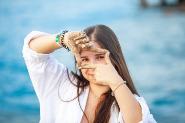 Portre güzel Asyalı kadın gülümseyerek şapka takıyor. Tatil konseptinde sahilde ve denizde fotoğraf çektirirken mutlu mesut vakit geçiriyor. Yüksek kalite fotoğraf