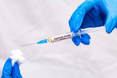 Hands in blue gloves holding a jar with a yellow vaccine. Typhoid Fever vaccination concept. close-up, selective focus. High quality photo clipart