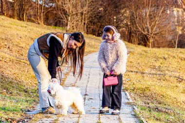 Doğanın koynunda güzel bir manzara parkın en güzel beyaz köpeğini gezdirirken iki güzel kızı yakaladı, çok mutlu ve heyecanlıydılar. Yüksek kalite fotoğraf