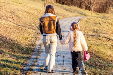 Güneşli bir bahar günündeki resim, iki kızın el ele tutuşarak yeşillenmeye başlayan parkta gezinirken şaşırdığını gösteriyor. Yüksek kalite fotoğraf