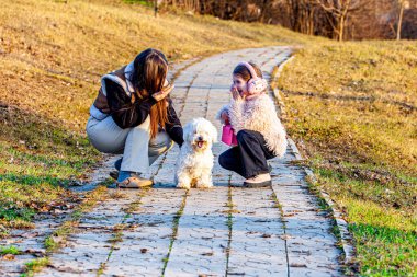 Bahar arka planında, doğanın kucağında çok renkli ve güzel renklerle çekilmiş bir resim. İki kız en iyi arkadaşları olan küçük beyaz köpekle oynuyorlardı.