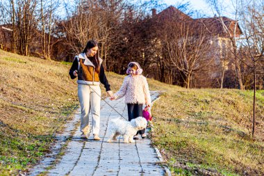 Resim çok güzel bir parkta çekildi. Şimdi yeşile dönüyordu ve güneş parlıyordu. Kızlar beyaz köpekleriyle oynuyorlardı ve çok mutluydular. Yüksek kalite