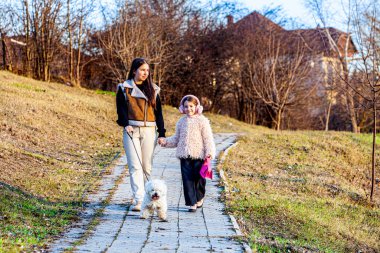 Resim çok güzel bir parkta çekildi. Şimdi yeşile dönüyordu ve güneş parlıyordu. Kızlar beyaz köpekleriyle oynuyorlardı ve çok mutluydular. Yüksek kalite