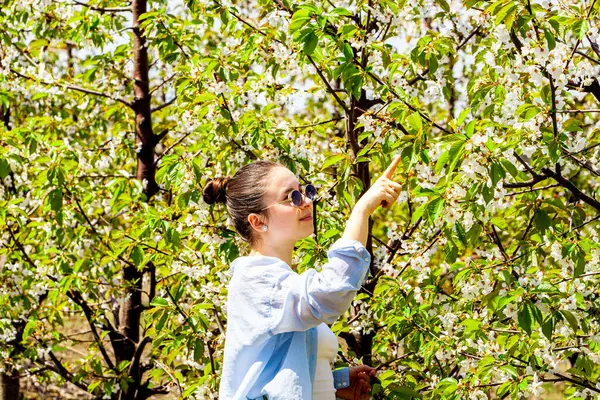 Akan beyaz elbiseli esmer kadın pembe kiraz çiçekleri kokan güneşli baharda çiçek açan ağaçların arasında duran doğal çevreyle barışçıl bağını ifade eden. Yüksek kalite fotoğraf