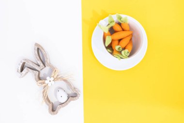 Top view aerial image of decoration and simbol of Easter holidays. Bunny and carrotts in white cup.White and yellow backgrounds with copy space.