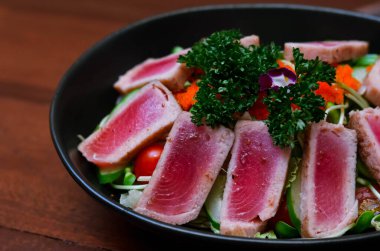 Fresh tuna salad served with sunflower sprouts and fresh organic lettuce in an elegant black plate placed on a wooden table and old newspapers.