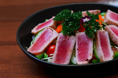 Fresh tuna salad served with sunflower sprouts and fresh organic lettuce in an elegant black plate placed on a wooden table and old newspapers.