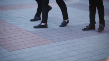 Arka planda güneş ışığıyla yürüyen üç iş adamının bacakları. İş adamları yaya geçidinde yürüyor. Yaklaş.