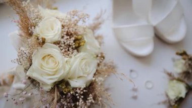 Güzel bir buket gül ve kurutulmuş çiçekleri boho stili bir düğünle süslenmiş masanın üzerinde. Bulanık ayakkabı ve yüzükler masada nişan için.