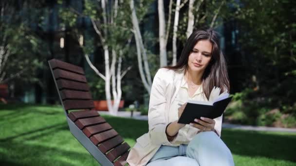 緑の春の公園の庭に屋外に座っている間インスピレーションを探しています 若い女性は彼女の希望と未来の夢を日記に書き 計画を立てている 実行するプランナー — ストック動画
