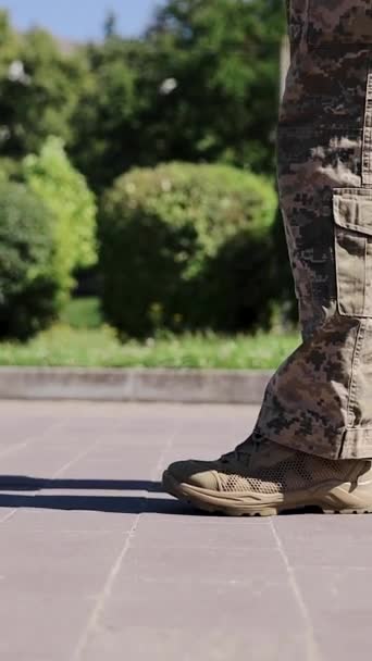 ストリートを歩く男性兵の足に続く側面の景色 カモフラージュの軍服を着た男が歩行者ゾーンにいる 都市歩道を歩く低角度の脚 バーティカルビデオ — ストック動画