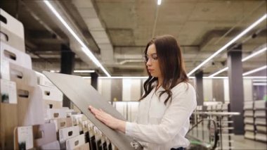 Elinde parke pano örneği tutan bir kadın. Genç bir kadının eli, bir hırdavatçıdaki plastik zemini inceliyor.