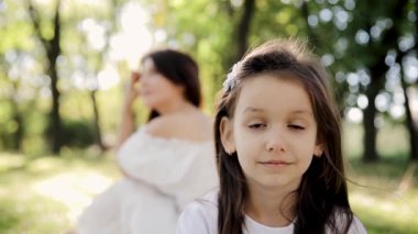 Güneşin altında bir çocuğun mutlu yüzü. Ön planda bir kızın portresi ve parkta arka planda bulanık bir annesi. Anne ve kızı.