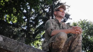 Bir Ukraynalı asker düşünceli bir şekilde uzaklara bakar. Adam taktik gözlük takıyor. Ukrayna Silahlı Kuvvetleri. Üniformalı adam ellerini kavuşturdu.