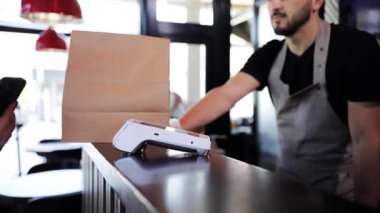 Bir kafede yemek ısmarlamak için kullanılan NFC ödeme teknolojisiyle akıllı telefon tutan kadınsı bir elin fotoğrafını çek. Müşteri yemek parasını kredi kartı terminali üzerinden ödemek için cep telefonu kullanıyor.