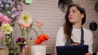 Beyaz kadın mağaza sahibi, önlük giyiyor, çiçekçide çalışıyor. Envanter sayımı için dijital tablet kullanan mutlu genç kadın çiçekçi. Küçük işletme, girişimcilik konsepti