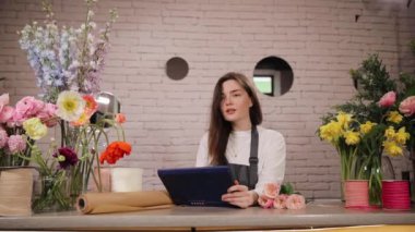 Çekici beyaz kadın mağaza sahibi önlük giyiyor, çiçekçide çalışıyor. Envanter sayımı için dijital tablet kullanan mutlu genç kadın çiçekçi. Küçük işletme, girişimcilik konsepti