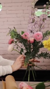 Kadın bukete yeni çiçek ekliyor. Kafkas kadın çiçekçi yarım bir düzenleme yapıyor ve kompozisyona bitkiler ekliyor. Tasarım, çiçek atölyesi, çalışma konsepti. Dikey video