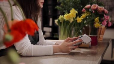 Çiçek buketi satan kadın çiçekçi. Güzel, rahat bir çiçekçide ödeme terminali tutuyor. Maaş kartı veya kablosuz NFC teknolojisi