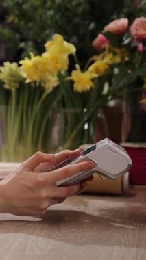 Çiçek buketi satan kadın çiçekçi. Güzel, rahat bir çiçekçide ödeme terminali tutuyor. Maaş kartı ya da kablosuz NFC teknolojisi. Dikey video