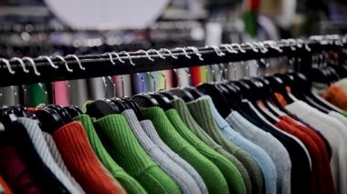 Renkli kazaklar, mağazadaki bir askıya düzgünce asılmış. Alışverişçiler için çeşitli örgü kıyafetleri sergiliyorlar. Müşteriler için canlı kıyafetler, askılarda asılı yün kazaklar.