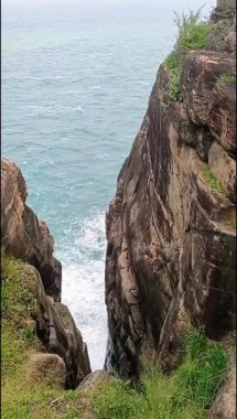 Trincomalee 'deki büyük bir kıyı kayası tarafından çerçevelenmiş sonsuz okyanusun barışçıl manzarası deniz ve gökyüzüne açılan doğal bir portal yaratıyor ve dalgalar uzaklarda yankılanıyor.